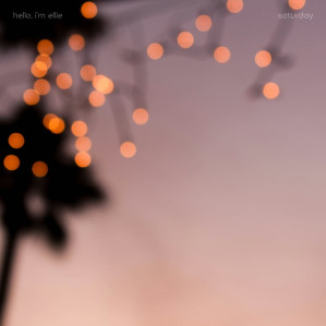 An out-of-focus image of some fairy lights that are hanging on the edge of a roof of a beach hut (I think). It's at sunset, and a blurry palm tree is visible at the left of the image. 'hello, i'm ellie' is at the top left, and 'saturday' is at the top right.